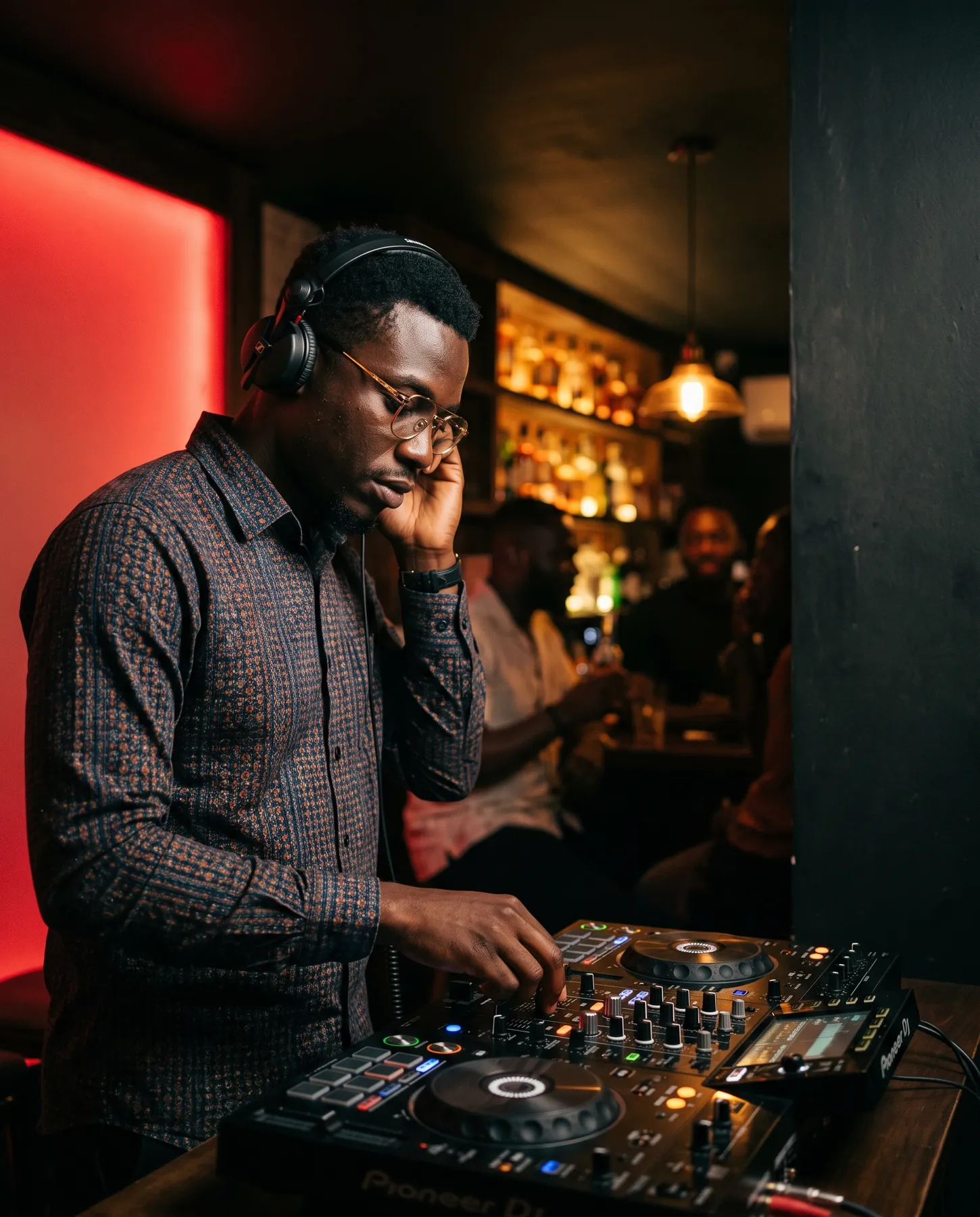 A DJ working a controller in a warm lounge with red wall glow behind